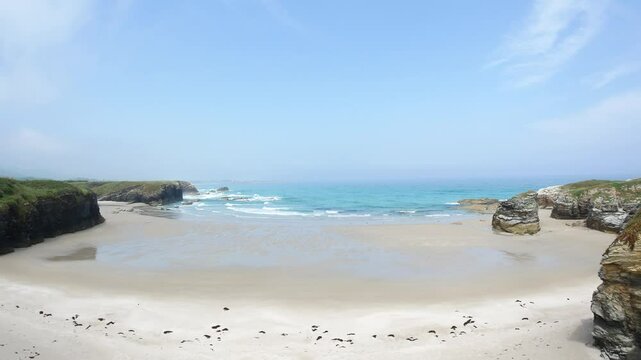 Low tide at As Catedrais beach Galicia Spain reveals sandstone rocks tidal pools reflecting sky cliffs lining wide shore under bright light peaceful calm natural wonder