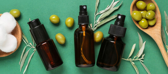 Bottles of natural cosmetic products, cotton balls and olives on green background