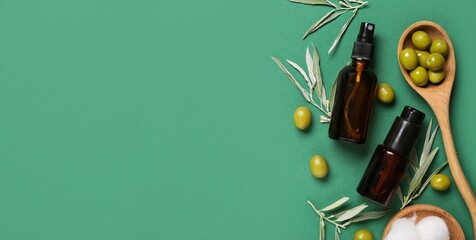 Bottles of natural cosmetic products and olives on green background with space for text