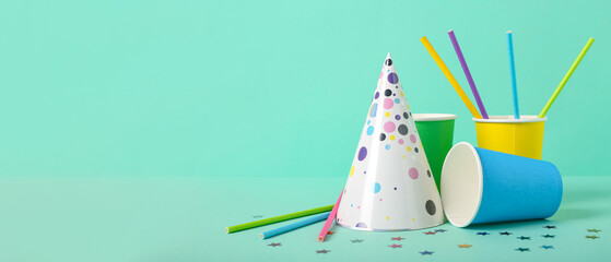 Party hat, cups and straws on turquoise background with space for text