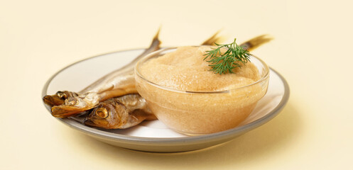 Plate with bowl of caviar and smoked capelin fishes on beige background