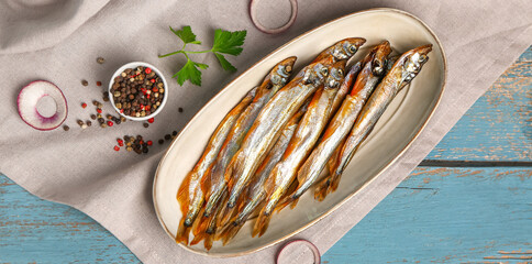Plate with tasty smoked capelin on blue wooden background