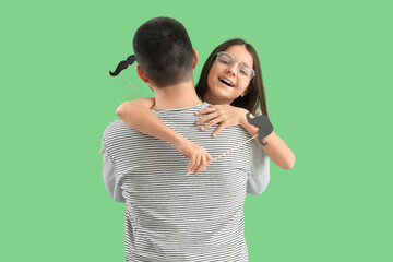 Portrait of hugging father and his little daughter with paper mustache on green background