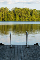Lake dock with swimming steps overlooking tranquil water and lush green trees. Serene recreational area perfect for swimming and relaxation activities