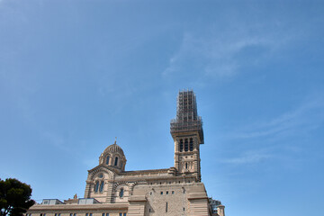 Notre Dame de la Garde Basilica in Marseille, France, with the tower under restoration under scaffolding and a clear blue sky in the background