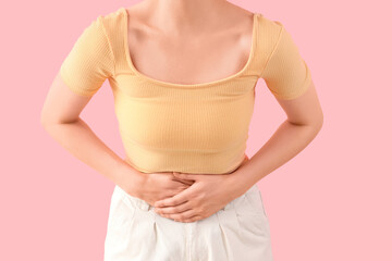 Young woman suffering from stomach ache on pink background, closeup