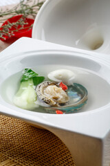 Abalone in clear soup in a white square porcelain soup plate