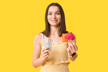 Beautiful young woman with contraceptive pills and condoms on yellow background. AID awareness concept