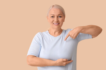 Mature woman checking her breast on beige background. Cancer awareness concept