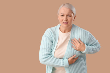 Mature woman suffering from breast pain on brown background. Cancer awareness concept