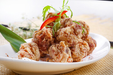 Fried chicken nuggets in a gooseneck porcelain plate are placed on a straw mat