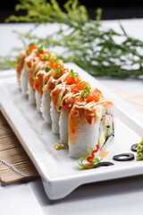 A salmon roll in a rectangular porcelain plate is placed on the sushi curtain