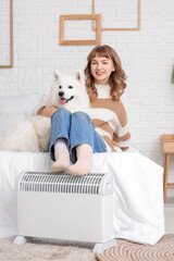 Young woman with cute Samoyed dog warming legs on radiator in bedroom