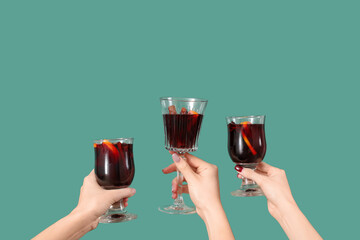 Female hands with glasses of warm mulled wine on green background