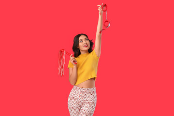 Beautiful young sexy Asian woman with whip and handcuffs on red background