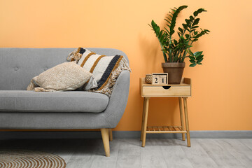 Grey sofa with cushions, houseplant and cube calendar on stool near peach wall