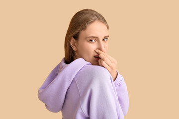 Young woman feeling disgusting smell on beige background