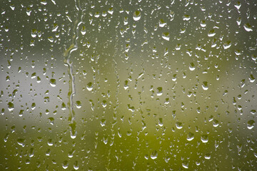 Raindrops cascade down a window, creating a tranquil view with a blurred green backdrop.