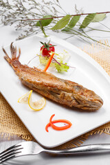 Japanese style grilled yellow croaker in a square porcelain plate placed on a straw mat