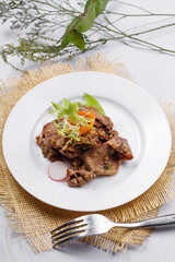 Round white porcelain plate of sizzling beef tongue with garlic sauce placed on a straw mat