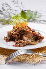Round white porcelain plate of sizzling beef tongue with garlic sauce placed on a straw mat