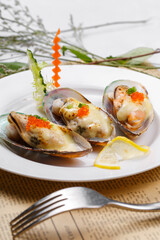 Baked mussels with mozzarella cheese in a round porcelain plate on English wrapping paper