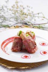 French foie gras beef rolls on a white round plate placed on a straw mat