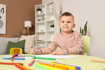 Funny little boy drawing with felt-tip pens at table in room