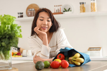 Young Asian woman and blue shopper bag with groceries in kitchen