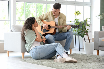 Happy young couple playing guitar at home