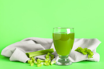 Glass of celery juice with chopped and whole celery on green background