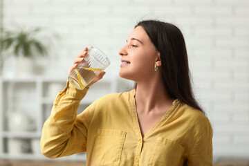 Beautiful young woman drinking lemon infused water in kitchen