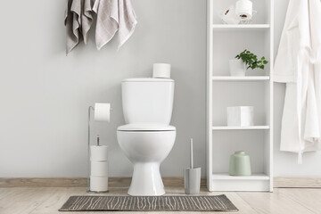 Toilet bowl, shelving unit, robe and towels in restroom
