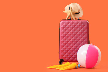Suitcase, inflatable ball and flip-flops on orange background. Travel concept