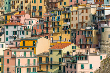 Pastel houses with balconies, green shutters, and hanging laundry line the hillside in Manarola,...