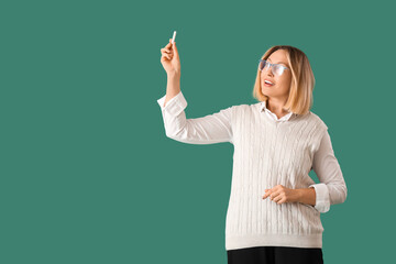 Mature female math teacher holding chalk on green background