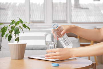 Woman pouring water from bottle into glass on table at home, closeup