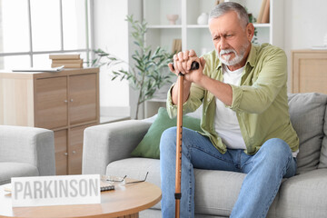 Senior man with stick suffering from Parkinson syndrome on sofa at home
