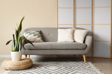 Interior of living room with grey sofa, plant and folding screen