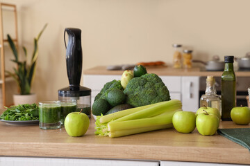 Glasses of healthy green smoothie with different fresh vegetables and fruits on table in kitchen