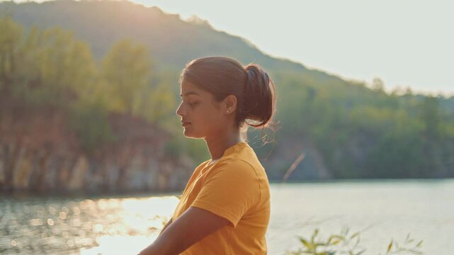 lotus position, young woman meditating with gyana mudra near a lake.