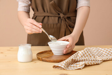 Woman with bowl of tasty yogurt and spoon at table on brown background