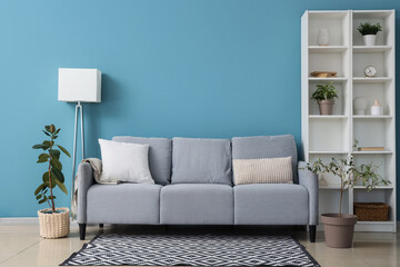 Comfortable sofa, houseplant and shelving unit near blue wall in room