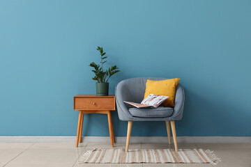 Cozy armchair with bedside table and houseplant near blue wall in room
