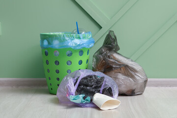 Trash bin and full garbage bags near green wall