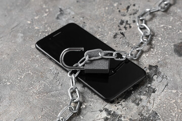 Open padlock with chain and mobile phone on grunge background, closeup. Cyber security concept