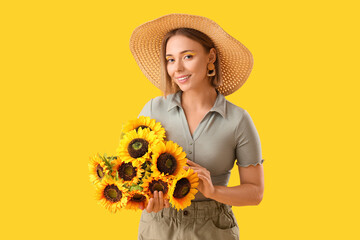 Beautiful young happy woman in wicker hat with stylish makeup and bouquet of sunflowers on yellow...