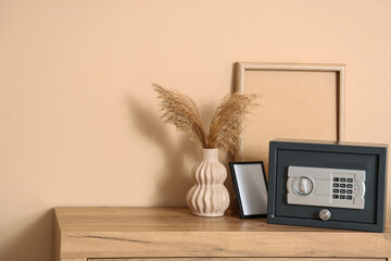 Modern safe, frame and vase with pampas grass on commode near beige wall