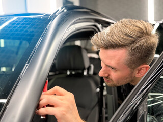 A car wrapping specialist applies a polyurethane film to the car. Detailer smoothes PPF. Car wrapping, detailing, tuning and styling. Selective focus. Car detailing and wrapping workshop. 