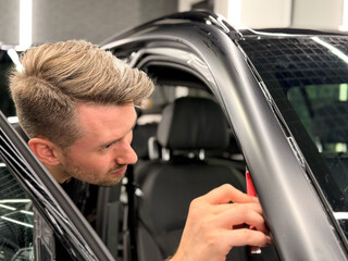 A car wrapping specialist applies a polyurethane film to the car. Detailer smoothes PPF. Car wrapping, detailing, tuning and styling. Selective focus. Car detailing and wrapping workshop. 